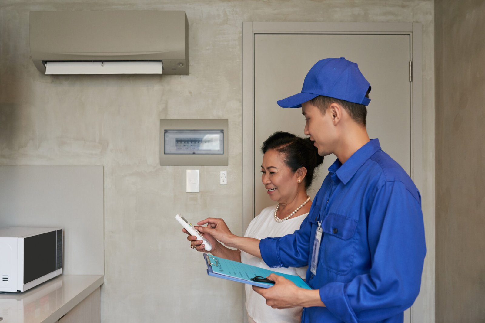 Technician explaining senior Vietnamese woman how to use air conditioner